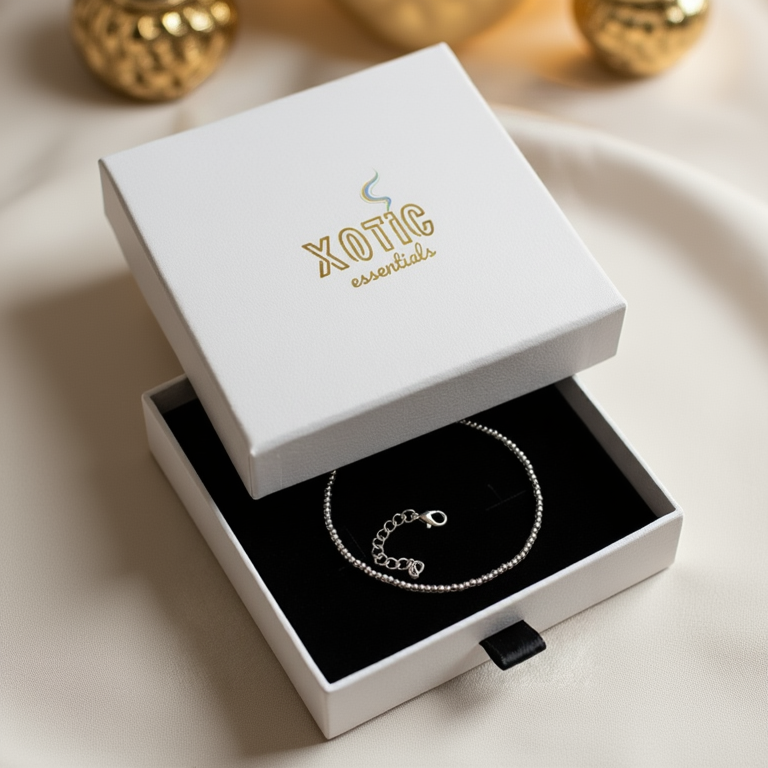 Silver bracelet in an open white box with 'Xotic Essentials' branding.