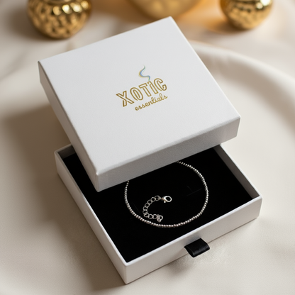 Silver bracelet in an open white box with 'Xotic Essentials' branding.
